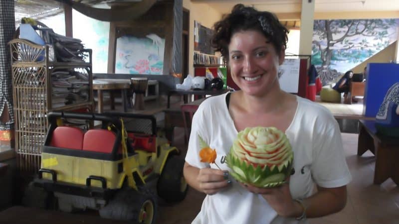 Photo of betternotstop founder Hannah Cox holding a melon carved into the shape of a rose in one hand and a rose in the other.