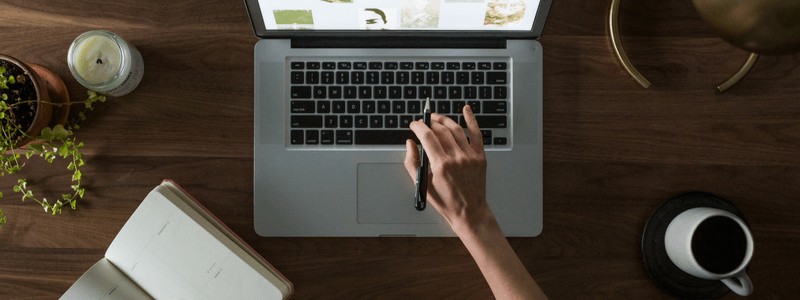 Photo of a hand holding a pen reaching over a laptop keyboard.