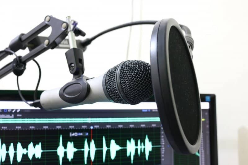 Photo of podcast equipment; microphone, computer screen with soundwaves visible on screen.